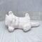 Handmade paintable ceramic cat on its back on a lacy ecru table cloth with a curtain behind it.